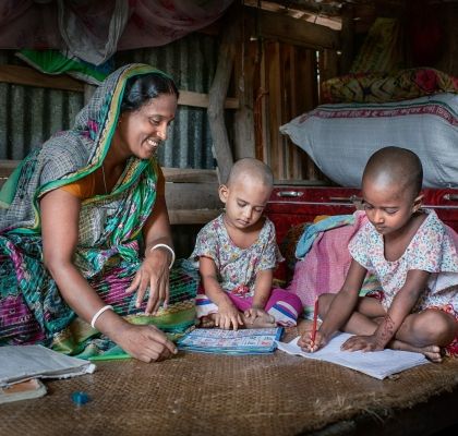 Mother helping her two children with their homework in Bangladesh
