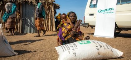 Woman and her child crouch above bag of grain distributed by Concern in Kenya 