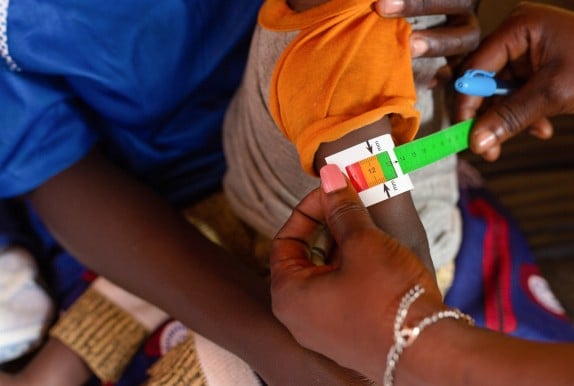 Concern health worker using mid-upper arm circumference tape on child