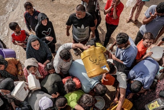 People gather with jerrycans and other containers to collect water from a tanker cistern in Deir el-Balah in the central Gaza Strip