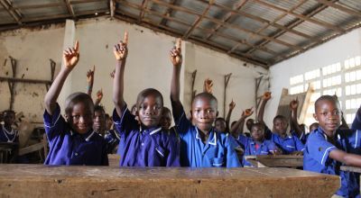 Children sitting in school classroom with hands in the air 