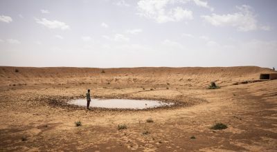 Man standing by nearly dry dam in middle of desert 