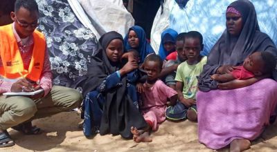 A woman sits in a camp surrounded by several young children
