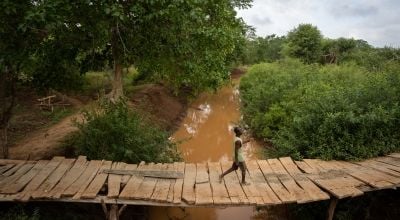 A man uses a small bridge to cross a river in Tana River County, Kenya