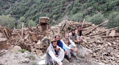 Four men sitting next to a completely collapsed building in Kunar Valley, Afghanistan