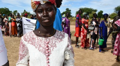 Ajok Deng, a woman in South Sudan wears a white dress, holding some cash. Behind her is a queue of people