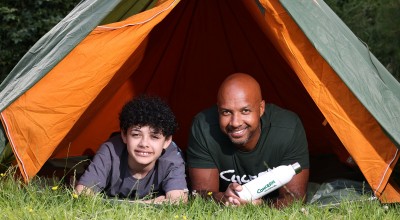 Two people, a man and an older child, in a tent outside looking straight ahead