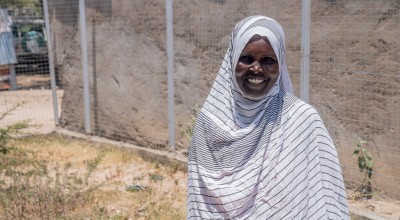 Woman smiling, stand outside wearing a white and grey striped head scarf