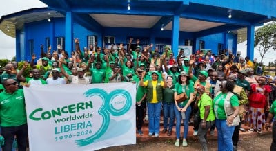 Around 60 people dressed in the green of Concern Worldwide, outside a blue building in Buchanan, LIberia.