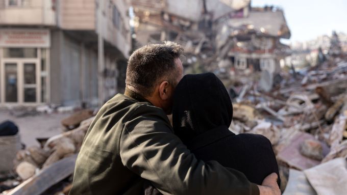 A man and woman embrace as they look at the rubble caused by the earthquakes in Turkey